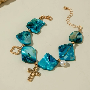 Detailed shot of bohemian ocean style bracelet with blue shell charms and gold cross pendant