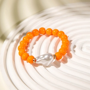 Detail of orange beads bracelet with silver baroque pearl on a white textured plate