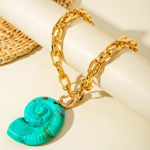 Collier à grosse chaîne dorée avec pendentif coquillage turquoise sur un tapis tissé