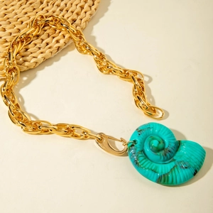 Gros plan détaillé d'un pendentif coquillage turquoise sur une grosse chaîne dorée