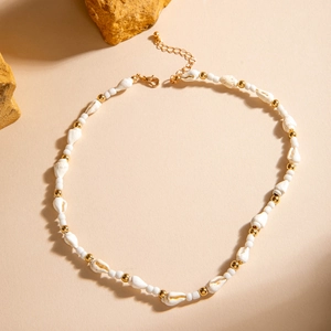 Detail einer Boho-Muschelkette mit weißen und goldenen Perlen auf sandigem Grund