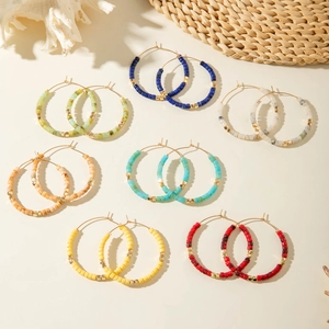 Détail de boucles d'oreilles bohèmes serties de perles en résine colorées et dorées