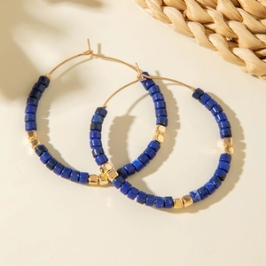 Détail de créoles dorées avec perles bleues texturées lapis et entretoises carrées