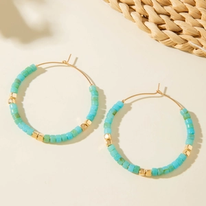 Détail de boucles d'oreilles créoles bohèmes avec perles de résine turquoise et métal
