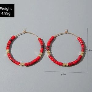Détail de boucles d'oreilles créoles françaises avec perles rouges et cubes dorés