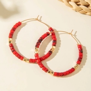 Détail de créoles en perles rouges avec accents dorés au style bohème