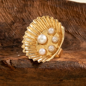 Detail of a golden shell ring with five pearls on a dark wood surface