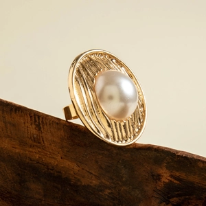 Macro detail of oval white pearl ring with textured golden radial metal base