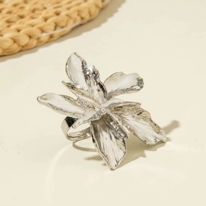 Detail of silver floral adjustable ring with textured petals on a beige surface
