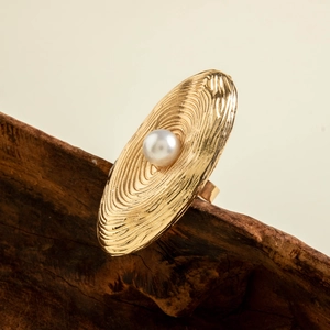 Macro detail of golden irregular flower ring with textured metal and pearl inlay