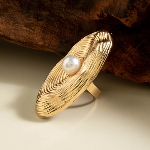 Macro detail of golden oval ripple ring with central pearl on a rustic wooden stand