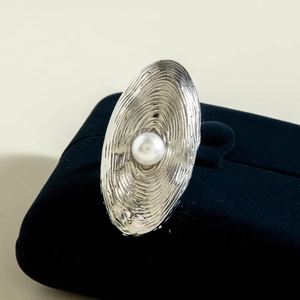 Macro detail of silver spiral oval ring with a central white pearl on black velvet