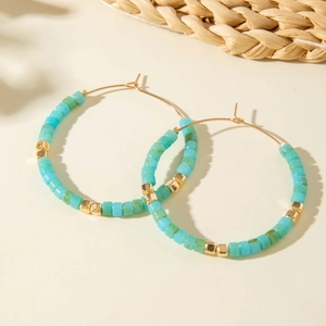 Créoles dorées bohèmes avec perles turquoise et accents dorés sur fond beige neutre