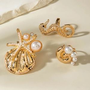 Detailed set of gold sea shell brooch and seahorse rings with pearls on stone background
