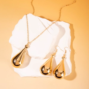Detail view of gold teardrop jewelry set featuring polished necklace and earrings on stone base