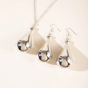 Detailed view of silver teardrop necklace and matching hook earrings set on light base