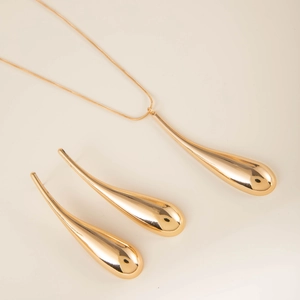 Macro shot of minimalist gold teardrop pendant and matching earrings with mirror finish