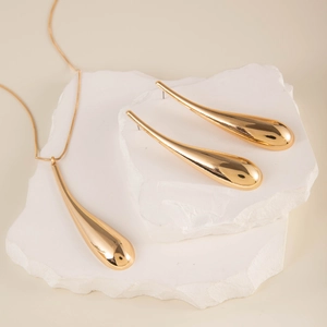 Detail of gold teardrop jewelry set featuring polished necklace and earrings on white stone
