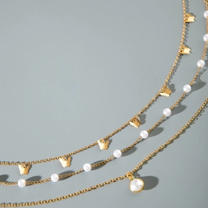 Close-up of multilayered gold body chain featuring butterfly charms and white pearls