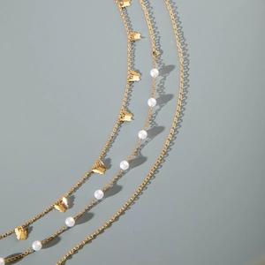 Detail of layered gold body chain with butterfly charms and white faux pearls