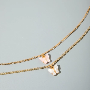 Detail of layered gold butterfly necklace featuring Figaro chain and crystal tennis chain