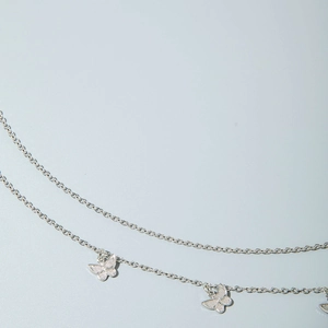Macro detail of silver layered waist chain with textured butterfly pendants on fine links