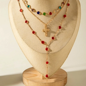 Detail of layered gold necklace with colorful stones and a cross pendant on a neck model