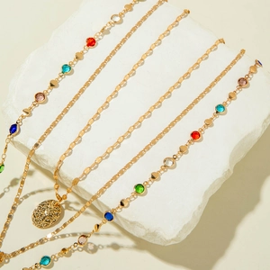 Detail of layered gold necklaces with colorful gemstones and textured oval pendant