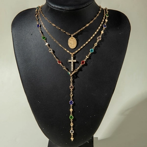 Detail of layered gold necklaces with cross pendant and multi-colored gemstone charms