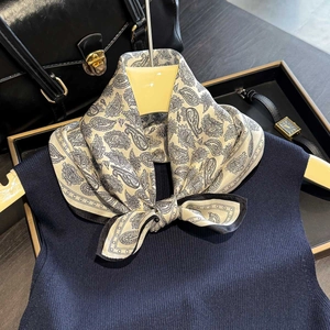 Beige silk scarf with black paisley pattern styled on a navy vest with luxury accessories