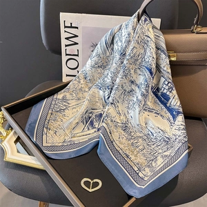 Blue and white silk scarf with landscape print and gold edges on a black tray