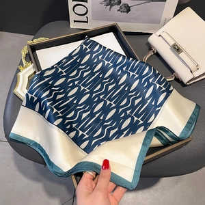 Silk square scarf with geometric alphabet print and dark green edges on a tray