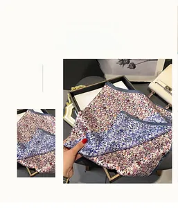Dettaglio di un foulard in seta con stampa floreale e bordo blu legato a una borsa