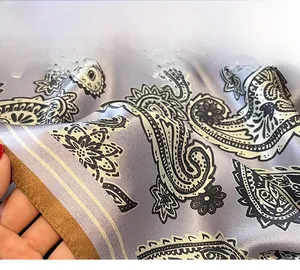 Macro detail of high-quality golden hemmed edges on a purple paisley silk neck scarf