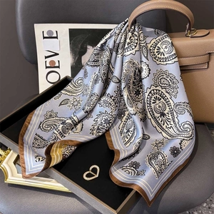 Carré en soie à motif paisley bleu-gris posé sur un sac en cuir et un magazine
