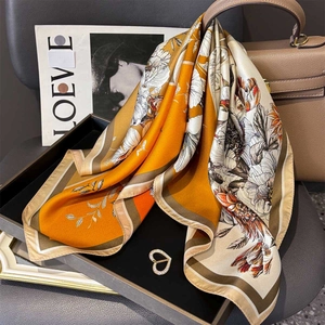 Elegant orange silk twill square scarf with floral print and heart brooch on a luxury bag