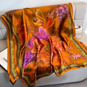 Orange floral silk shawl with peony prints displayed on a soft grey leather sofa