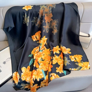 Elegant black silk-feel scarf with vibrant yellow floral print draped on a leather sofa