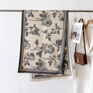 Detail view of beige scarf with black rose patterns, houndstooth edges and fine tassels