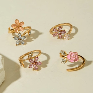 Set de 4 anillos dorados con flores, rosas rosas, cristales y perlas sobre fondo beige