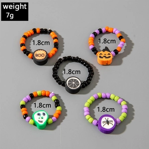 Detail of Halloween beaded ring set with pumpkin, skull, and spider charms on grey background