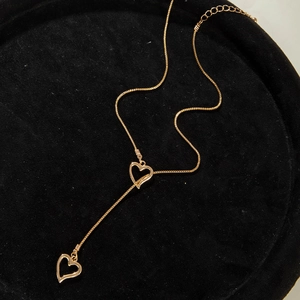 Vue détaillée d'un collier doré à double cœur en forme de Y sur présentoir noir