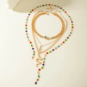 Detail of layered gold snake necklaces with colorful gemstones on a minimalist surface
