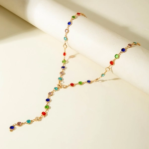 Macro detail of Y-shaped gold chain necklace with colorful faceted gemstones on a white pedestal