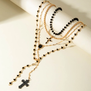 Layered gold cross necklace with black heart charms on cream display stand