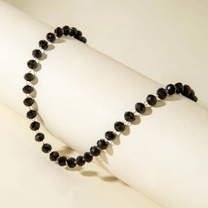 Detail of Y-shaped necklace with black faceted beads and gold wire on cylindrical display