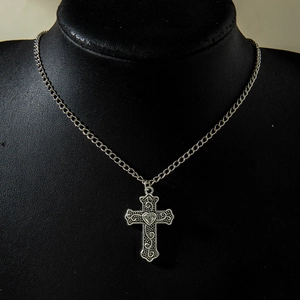 Detail of vintage silver cross pendant with heart center and intricate scrollwork on model