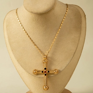 Close-up of gothic cross pendant with red and black stones on a gold chain
