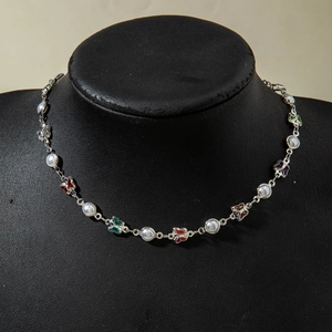 Détail d'un collier argenté avec des papillons multicolores et des perles blanches
