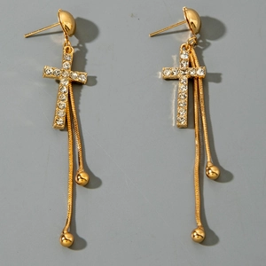 Détail de boucles d'oreilles croix dorées avec strass brillants et longues chaînes à franges